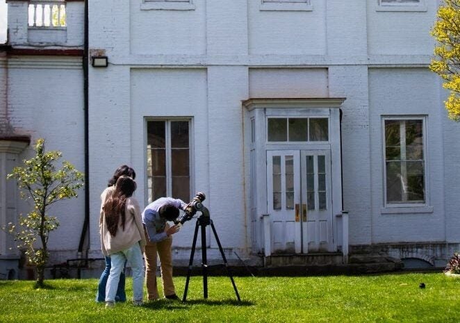Two students with a telescope outside of the observatory on a sunny day