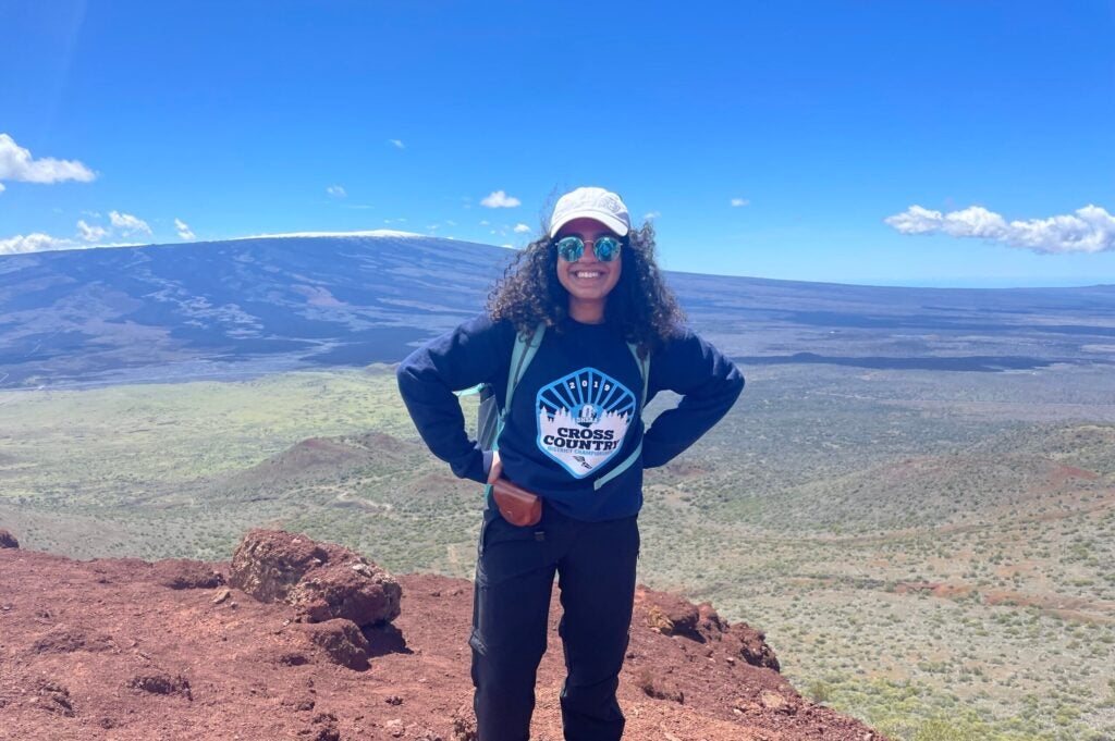 Kenzie Mounir stands on a ridge in front of Hawai'i's Mauna Loa volcano.